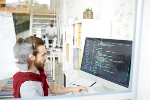 Serious programmer looking at coded data on computer screen while sitting in front of it