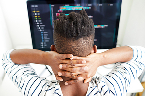 Rear view of busy African-American male software engineer checking code on computer and holding hands on neck