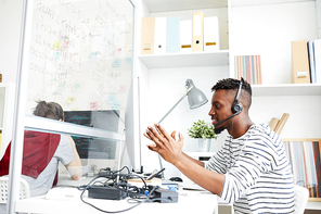 Young it-specialist in headset explaining someone details of technical problem while sitting in office