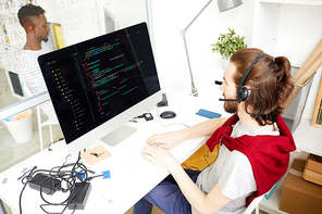 Young it-manager in headset sitting in front of computer monitor, talking to clients and working with data on screen