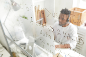 Programming code written on glassy board, African IT support operator in headset answering call and using computer in background