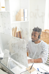 Serious and concentrated young it-manager sitting in front of computer monitor and answering questions of online clients