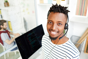 Smiling young office manager in headset looking at you while communicating with clients