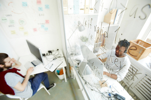 View of transparent board with written codes and two programmers working in office