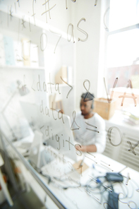 Written symbols of software language on transparent board in office of contemporary it-company