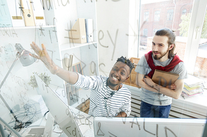 One of it-guys pointing at codes on board while discussing new computer language with colleague