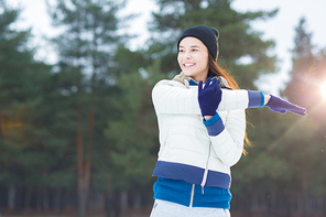 Healthy young woman in winterwear doing physical exercises in park