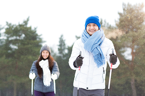 Happy guy in warm sportswear and his girlfriend on background skiing in forest or park