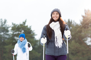 Happy young woman in warm winter jacket, white scarf, grey knitted beanie and furry mittens skiing on winter day with her boyfriend