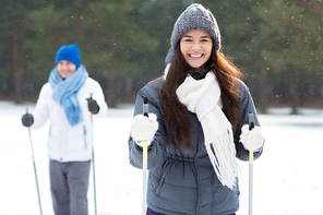 Happy young woman with toothy smile skiing in forest with her boyfriend at leisure