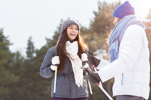 Laughing girl in winterwear looking at her boyfriend while skiing in snowfall