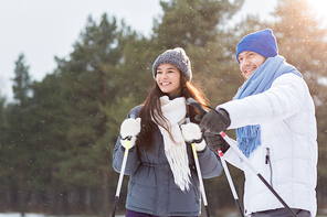 Young attractive couple in sportswear enjoying winter day in park while skiing
