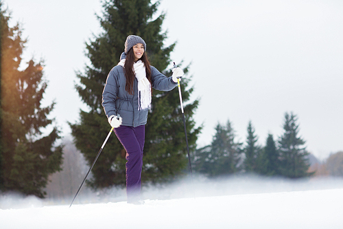 Winter girl in warm activewear skiing in park or forest on weekend