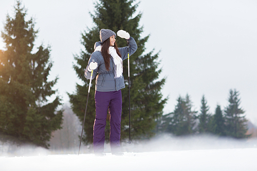 Young woman on skis looking afar while spending leisure in winter forest or park
