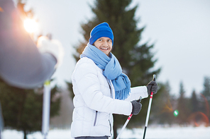 Happy young skier looking at his friend with smile during winter activity in park