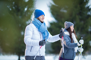 Young man and his girlfriend in warm activewear skiing in forest on weekend