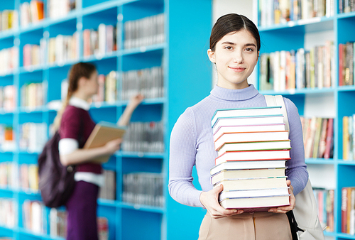 Successful student with stack of books and manuals going to take them in college library