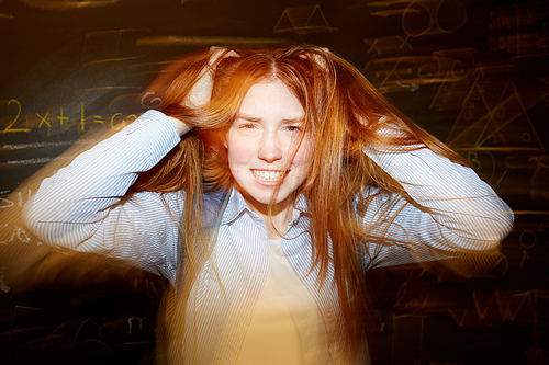 Smiling teenage girl ruffling her long ginger hair with hands and having fun