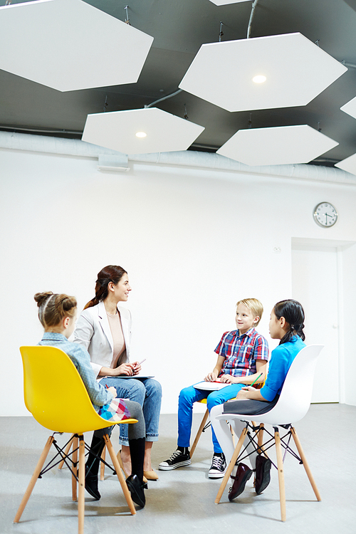 Cute schoolchildren and their teacher sitting in circle during lesson, brainstorming and voicing ideas