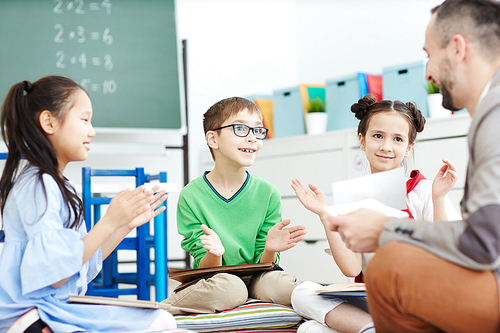 Elementary learners applauding to their teacher while learning at lesson