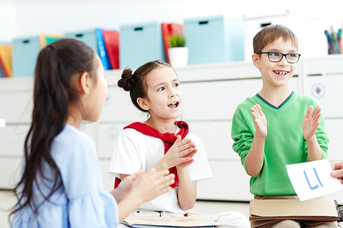 Group of elementary school kids singing songs and having fun while learning alphabet in classroom