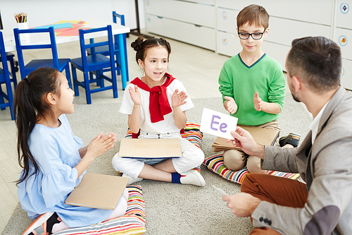 Three schoolkids sitting on the floor and playing english alphabet with teacher