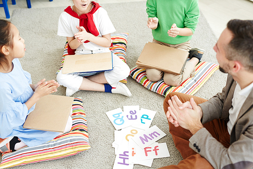 Primary school children and their male teacher sitting on the floor in classroom, playing games and learning alphabet letters