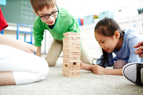 Elementary school kids sitting on the floor and playing with wooden block stack  after classes at school