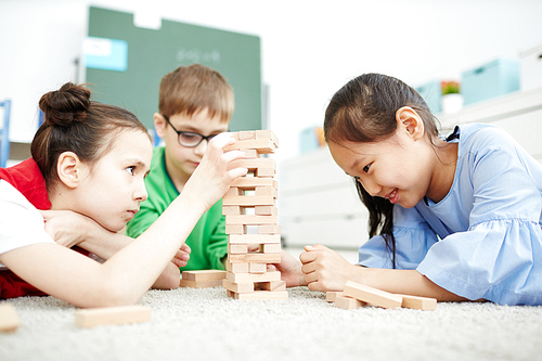 Multiethnic group of primary school children sitting on the floor in classroom and playing wooden block game during break
