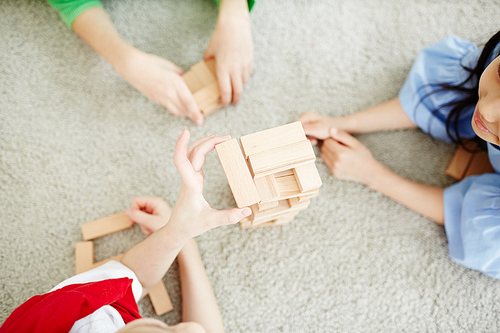 High angle view of little school kids building tower with wooden blocks while lying on carpet in classroom