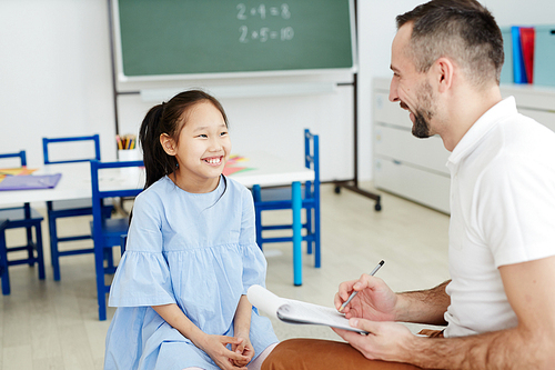 Cheerful schoolgirl looking at her teacher and listening to him during individual lesson