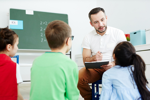 Contemporary teacher pointing at one of kids while listening to their answers