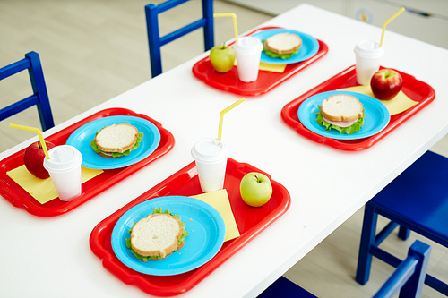 Fresh appetizing sandwiches, apples and drinks served on table in primary school canteen