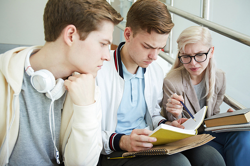 Blond girl pointing at text in book or manual while discussing the task with her groupmates