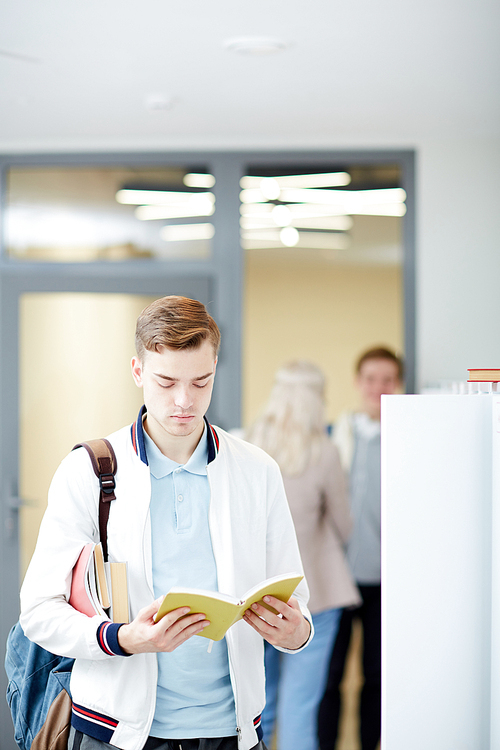 Serious guy with open book reading it in college library while preparing home assignment