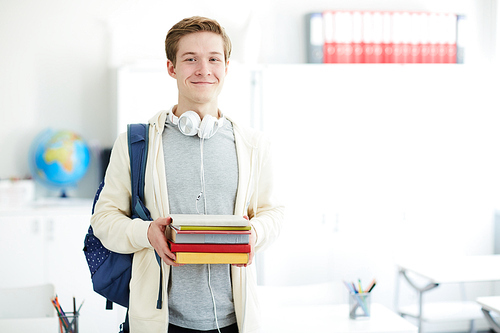 Happy young reader in casualwear holding several books that he has chosen in library