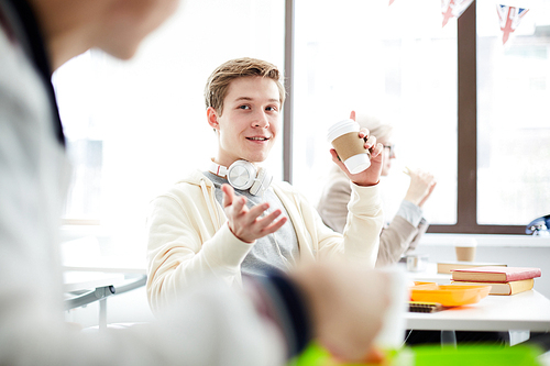 Casual guy with headphones talking to his groupmate while having drinks at lunch break