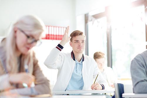 Smart guy in casualwear raising his hand to answer or ask question to teacher