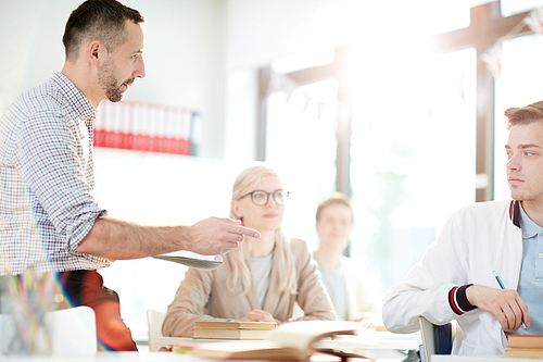 Teacher pointing at one of guys while asking questions to his students at lesson