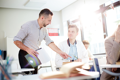 Clever guy looking at confident teacher and listening to his explanations while he pointing at notes