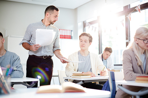 Teacher showing one of students paper with essay or test while passing them over