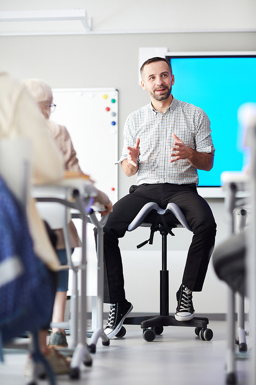 Young teacher in casualwear siting on chair in front of audience and introducing new topic to students