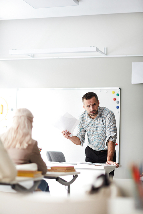 Serious or thoughtful teacher with papers leaning over his workplace in front of audience