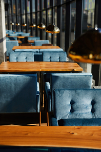 Long row of small tables and velvet chairs around them along windows inside cafe