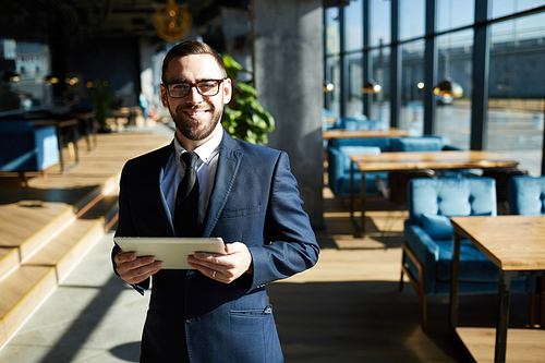 Cheerful man in suit using tablet while working in modern cafe on sunny day