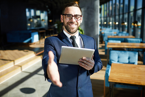 Businessman with toothy smile holding touchpad in one hand while giving the other one to client of cafe for handshake
