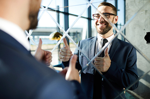 Successful businessman looking in mirror and showing thumbs up to himself