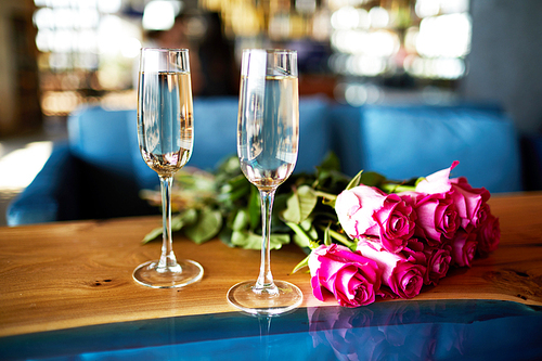 Two flutes of sparkling champagne and bunch or romantic fresh pink roses on wooden table in cafe