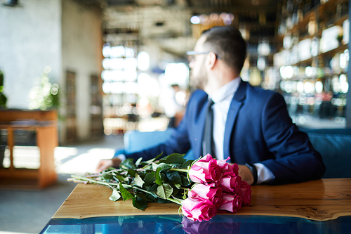 Fresh pink roses on table and elegant man sitting near by and waiting for his girlfriend