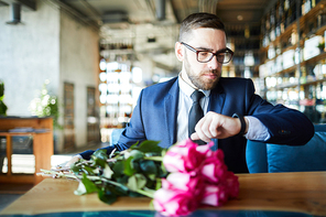 Young man looking at watch while waiting for his girlfriend in restaurant